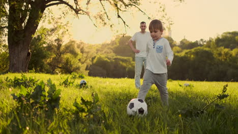 Padre-Parado-En-La-Puerta-Jugando-Al-Fútbol-Con-Su-Hijo-Al-Atardecer.-El-Padre-Entrena-Al-Niño-En-El-Campo.-Niño-Golpea-La-Pelota